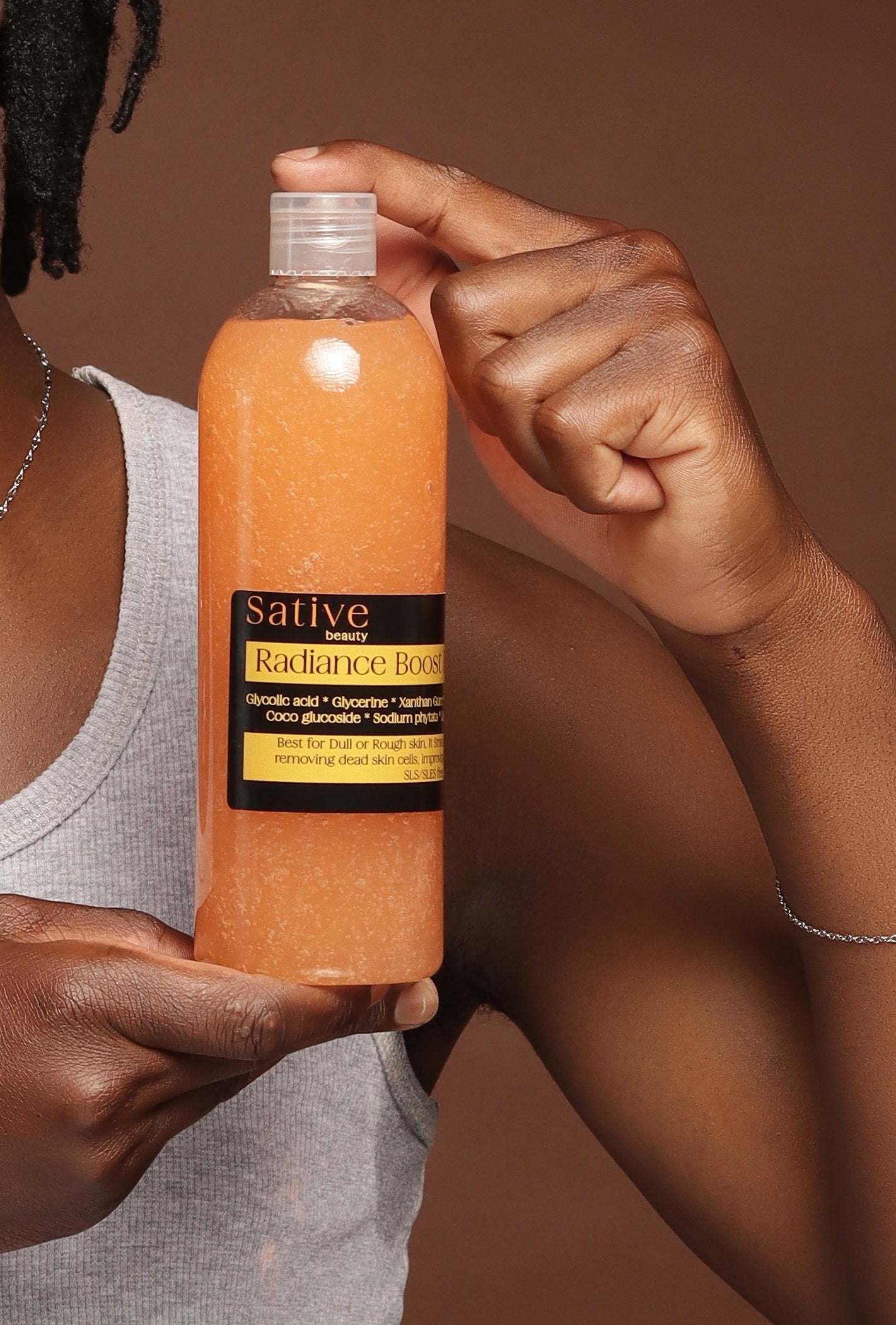 Person holding a bottle of Radiance Boost  Body Wash  against a brown background