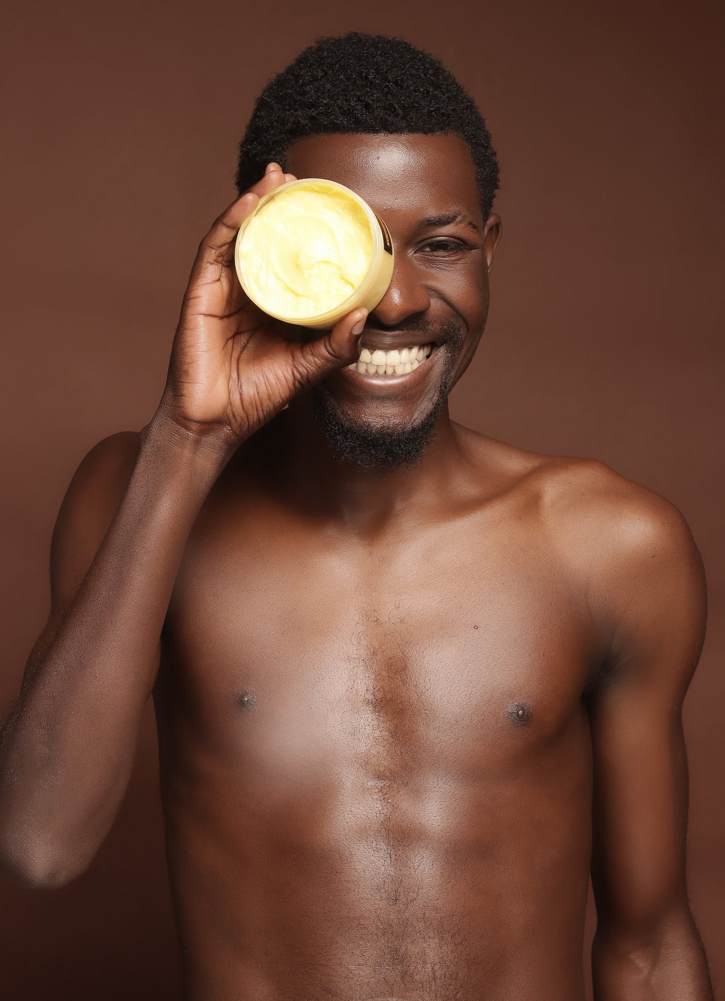Man holding Brightening Body Butter up to his eye against a brown background