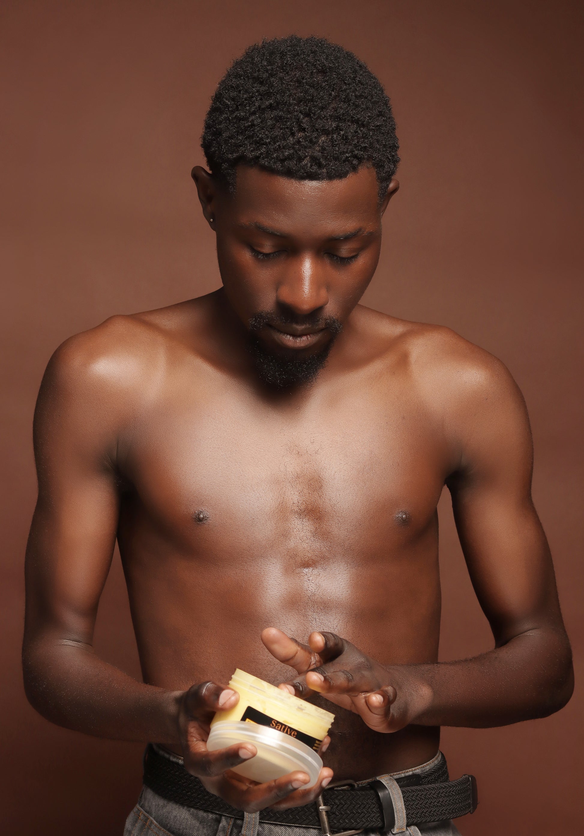 Man holding a jar of Brightening Body Butter against a brown background