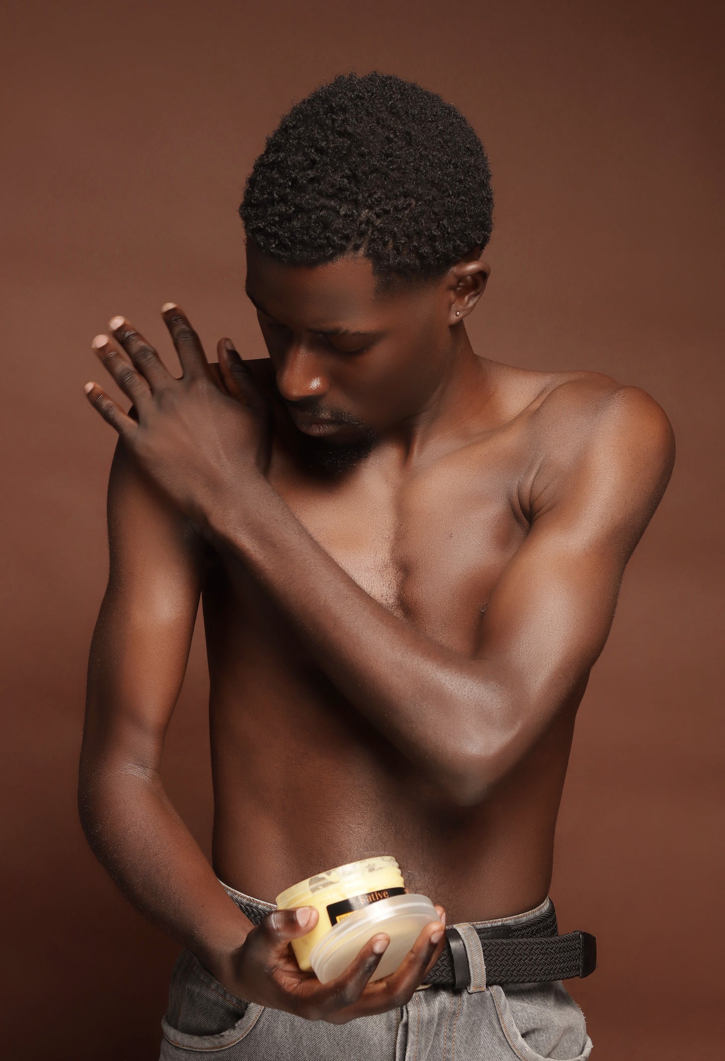 Man holding a jar  of Brightening Body Butter with a brown background