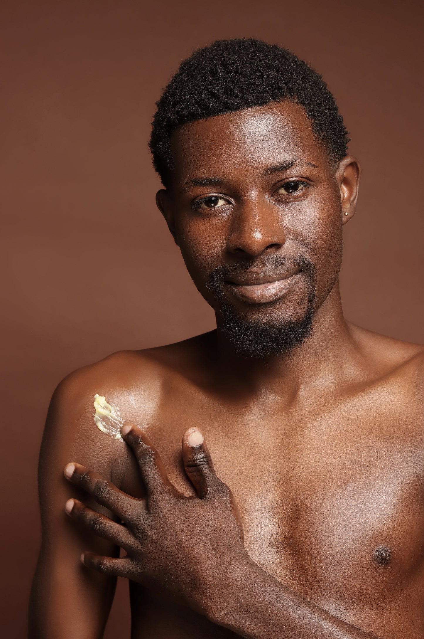 Man applying cream on his shoulder against a brown background