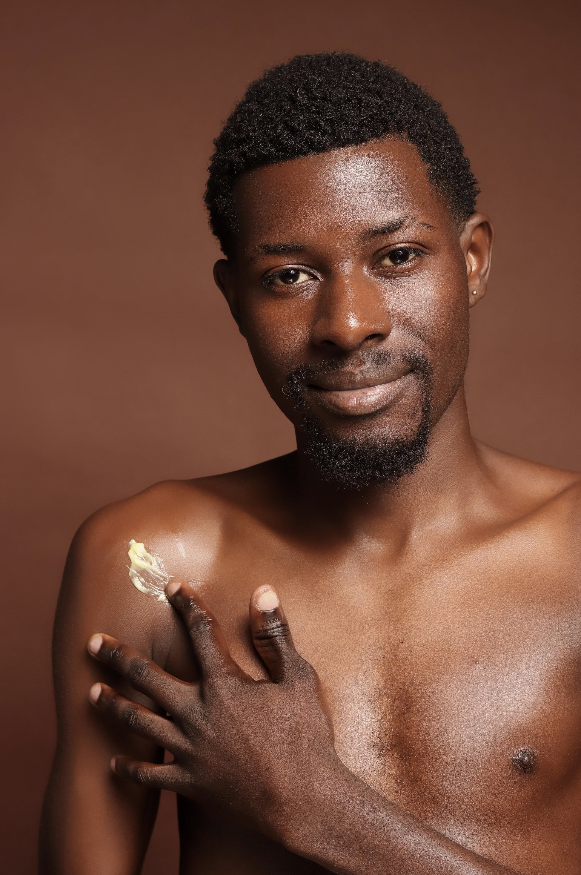 Man applying cream on his shoulder against a brown background