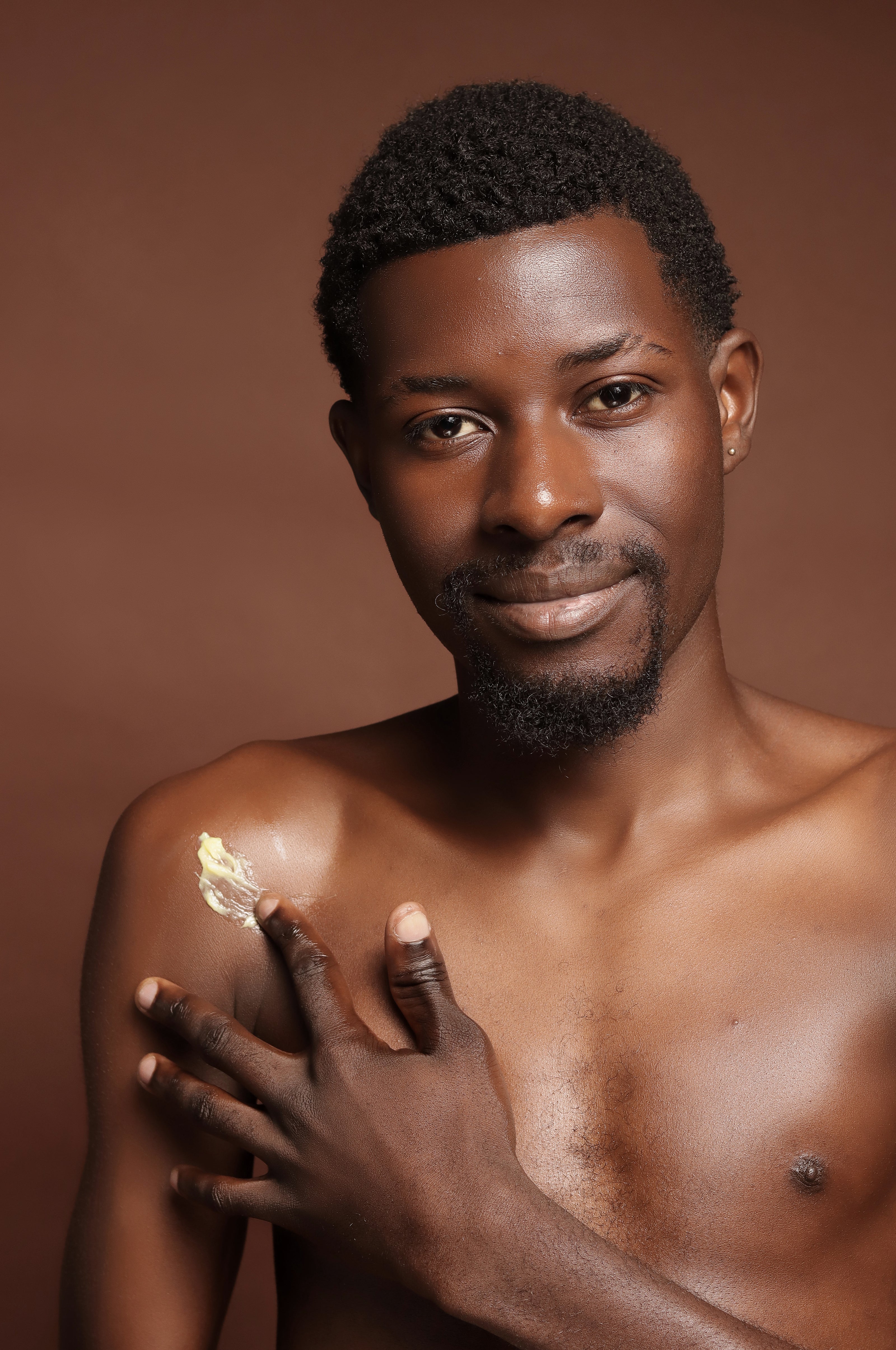 Man applying cream on his shoulder against a brown background