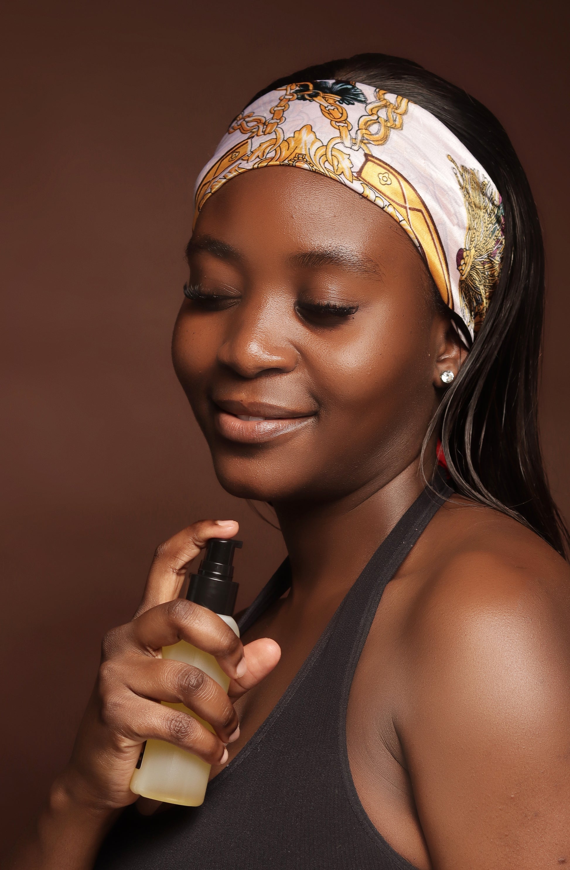 Woman holding a bottle of Pigmentation Correcting Body Oil  against a brown background