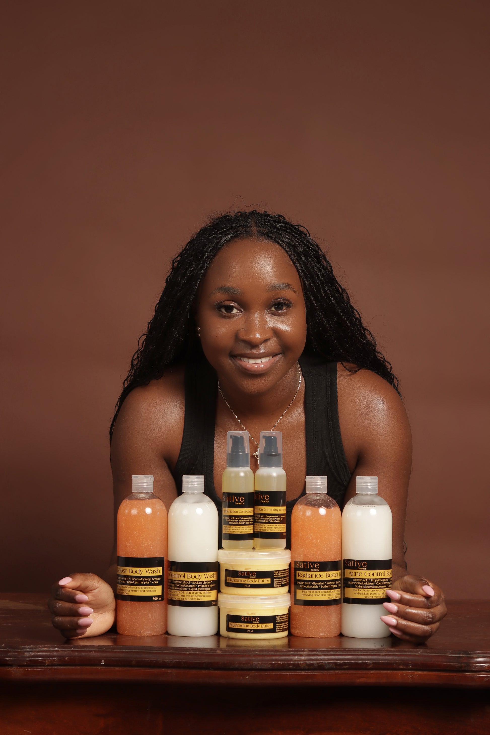 Woman posing with a variety of skincare products on a wooden surface against a brown background
