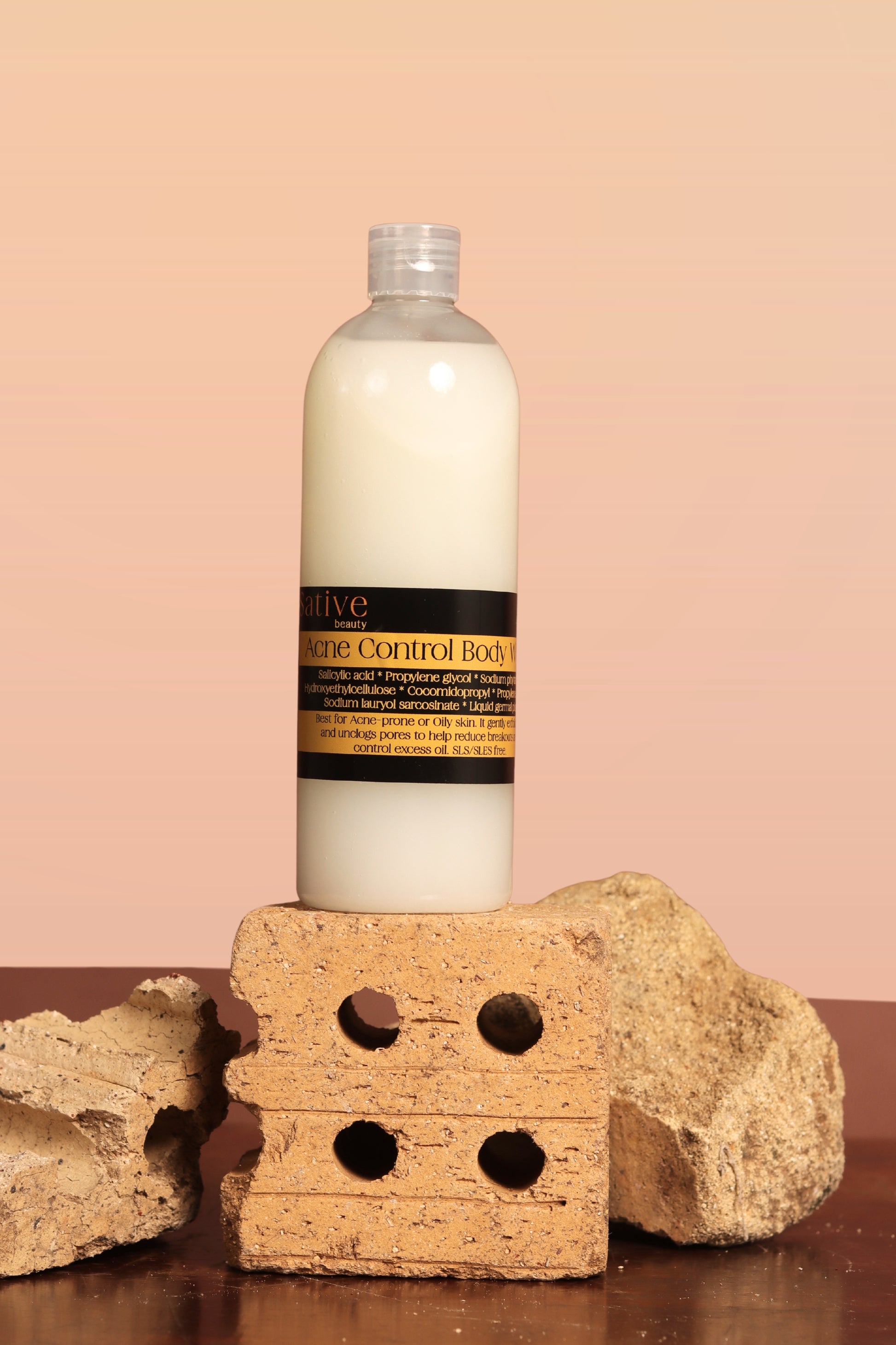 Bottle of Acne Control Body Wash on a stone block with a pink background