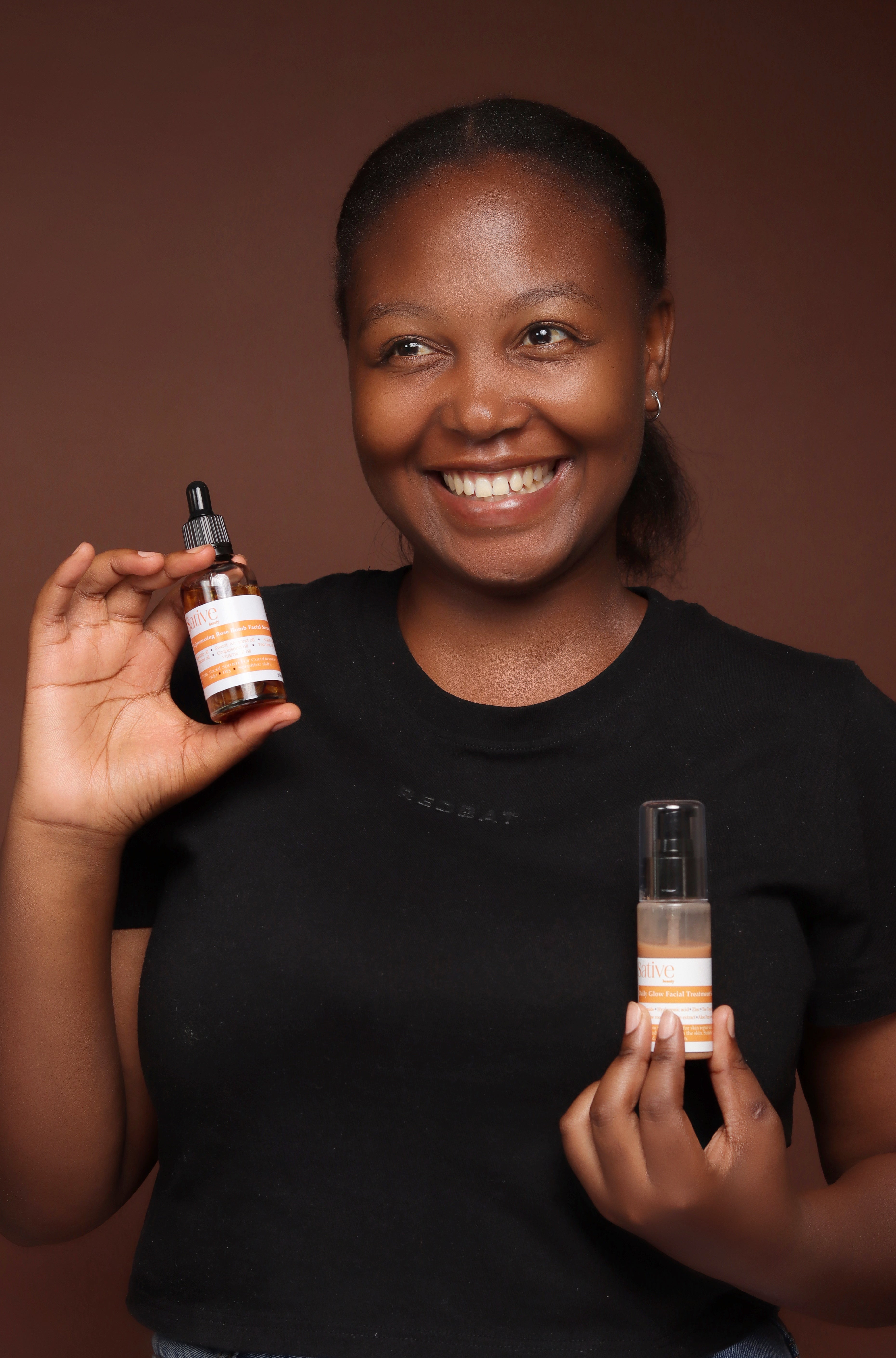 Woman holding two skincare products against a brown background