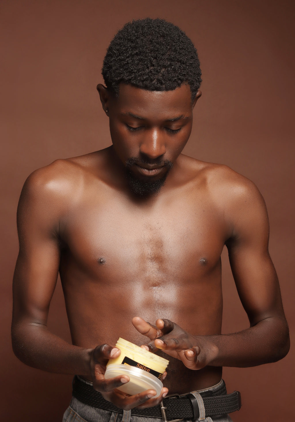 Man holding a jar of Brightening Body Butter against a brown background