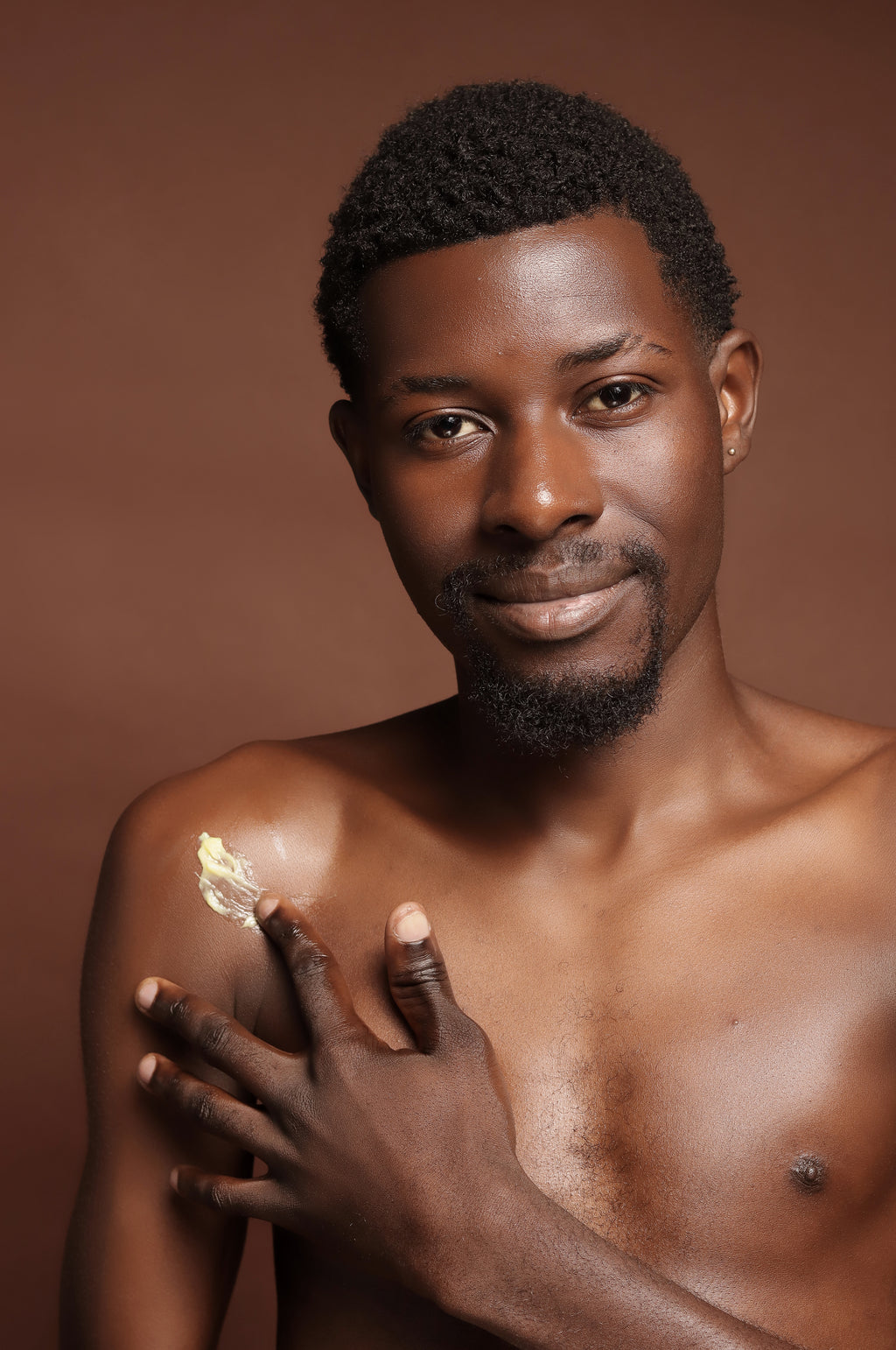 Man applying cream on his shoulder against a brown background