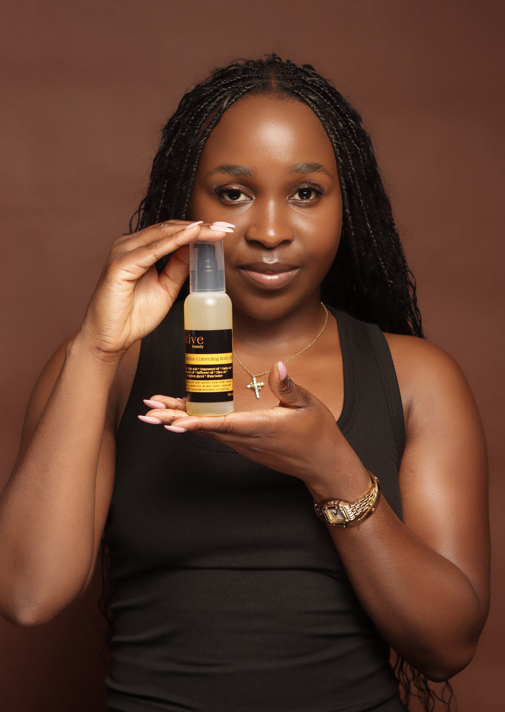 Woman holding a bottle of Pigmentation Correcting Body Oil  against a brown background