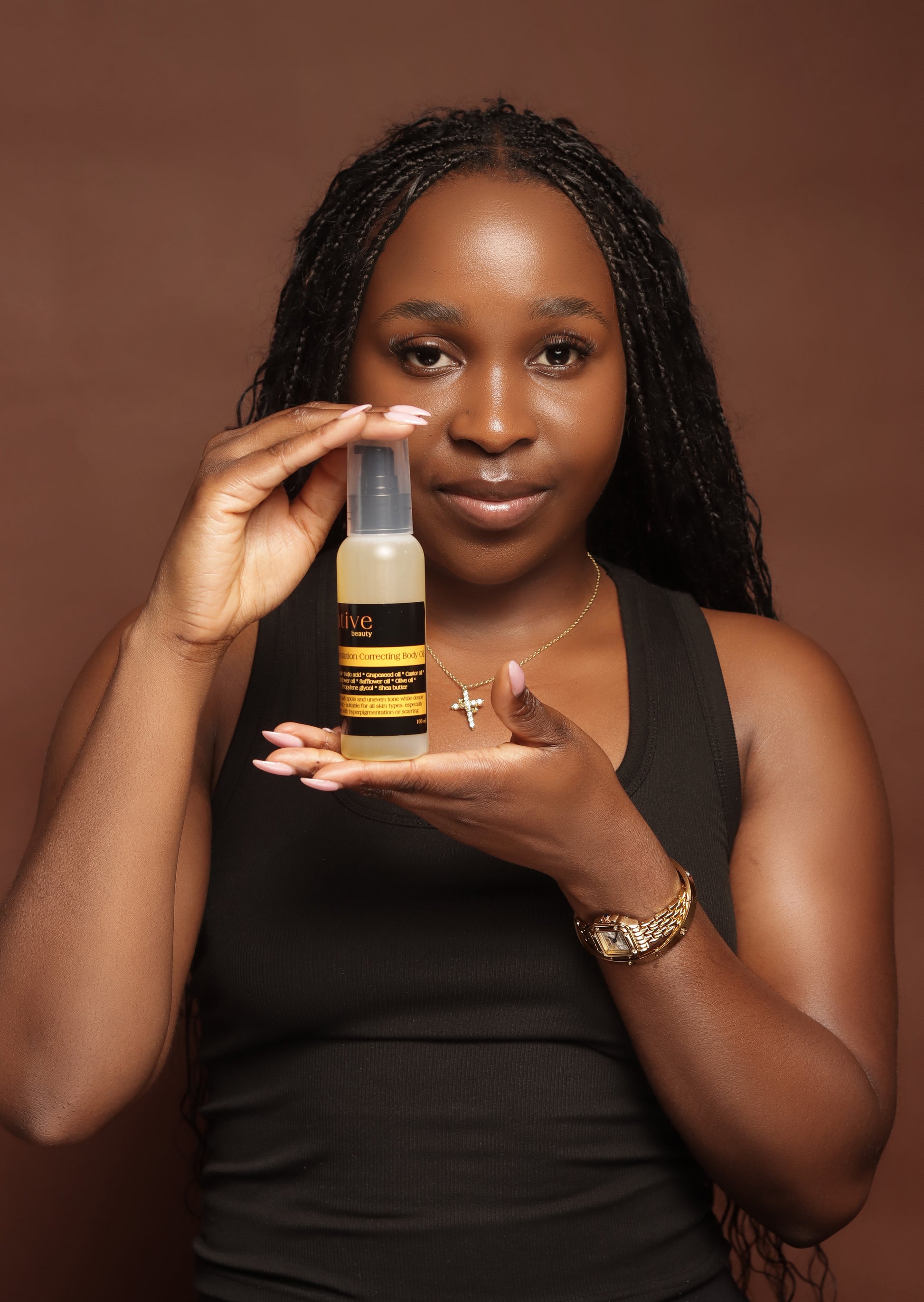 Woman holding a bottle of Pigmentation Correcting Body Oil  against a brown background