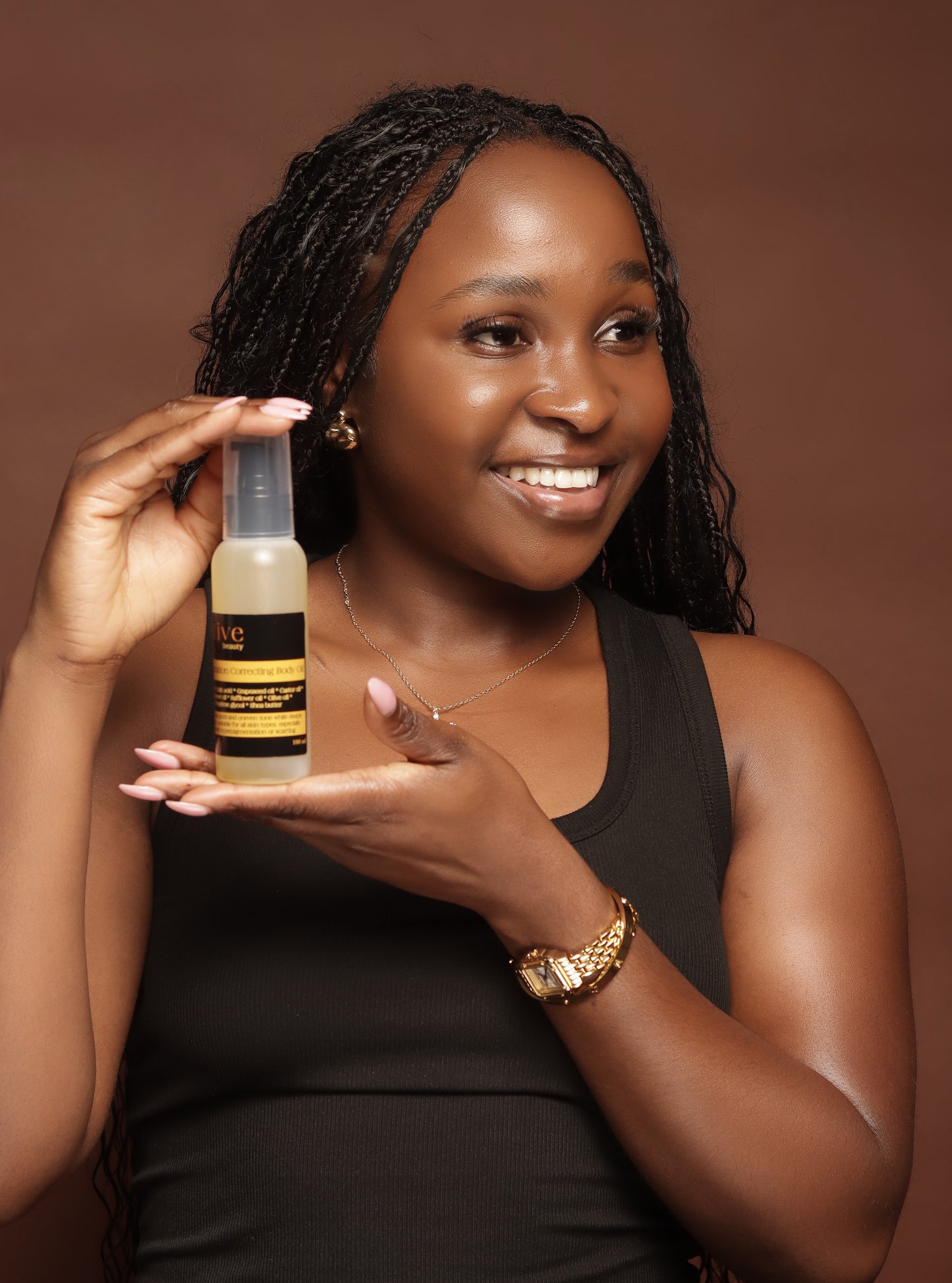 Woman holding a bottle of Pigmentation Correcting Body Oil  against a brown background